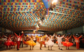 Traditional Festa Junina dancers in colourful outfits under festive flags during Brazil's June festivals celebration. 