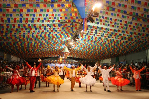 Traditional Festa Junina dancers in colourful outfits under festive flags during Brazil's June festivals celebration. 