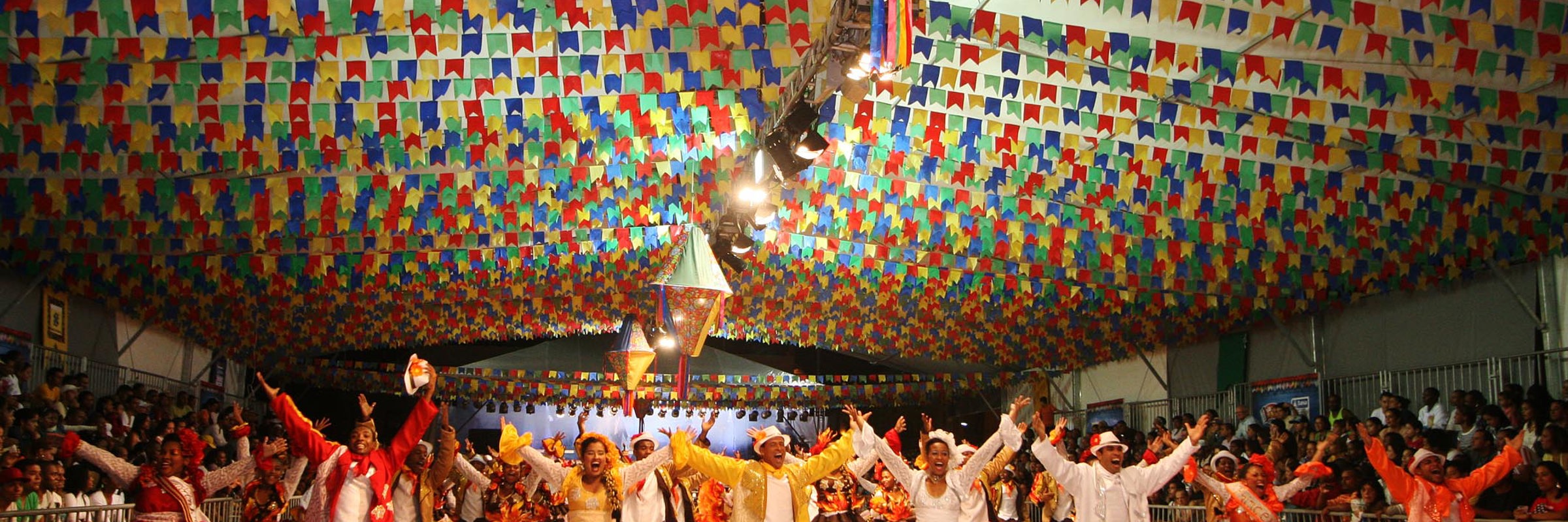 Traditional Festa Junina dancers in colourful outfits under festive flags during Brazil's June festivals celebration. 