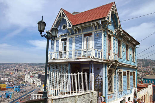 A traditional blue wooden house with ornate trim overlooks the hills and coast of Valparaiso, Chile.