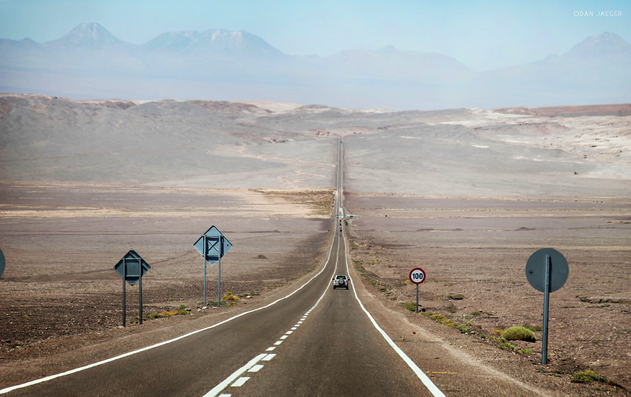Desert highway stretching into the Atacama landscape with mountains in the distance. 