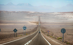 Desert highway stretching into the Atacama landscape with mountains in the distance. 