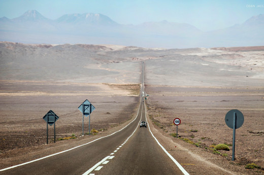 Desert highway stretching into the Atacama landscape with mountains in the distance. 
