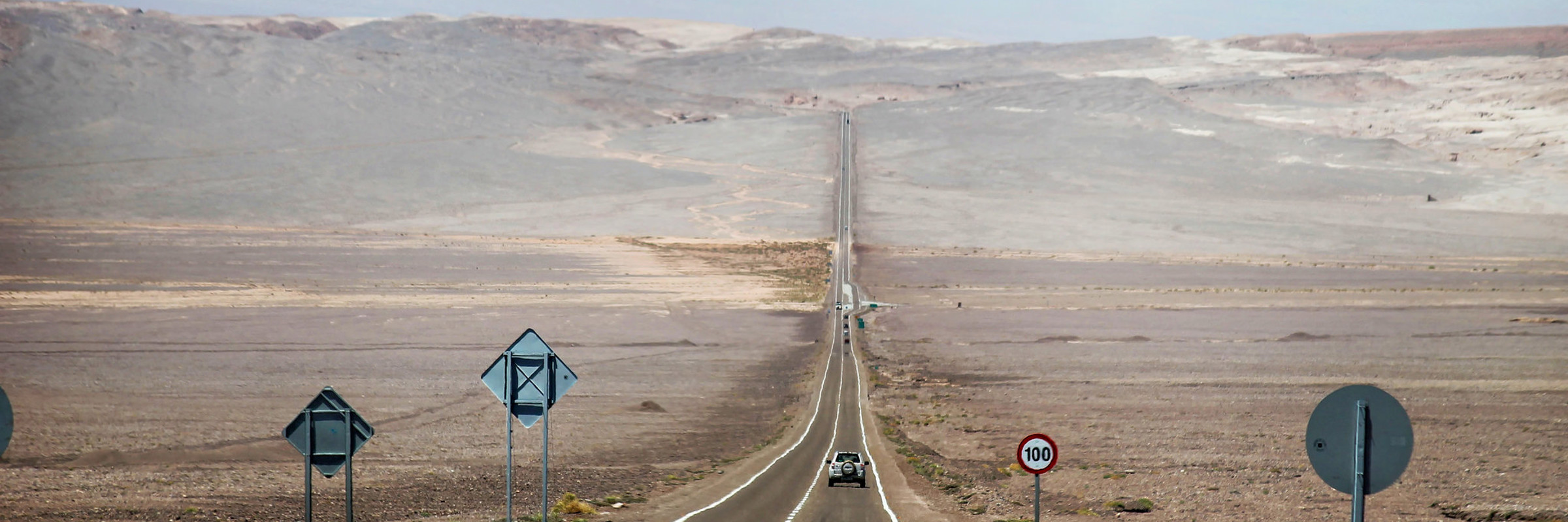 Desert highway stretching into the Atacama landscape with mountains in the distance. 