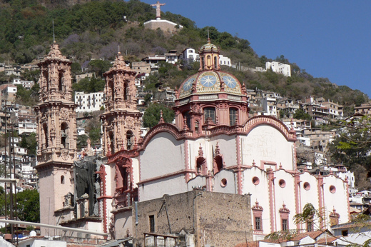 View of Santa Prisca Church in Taxco, a colonial silver town in Mexico, surrounded by hillside homes and scenic views. 