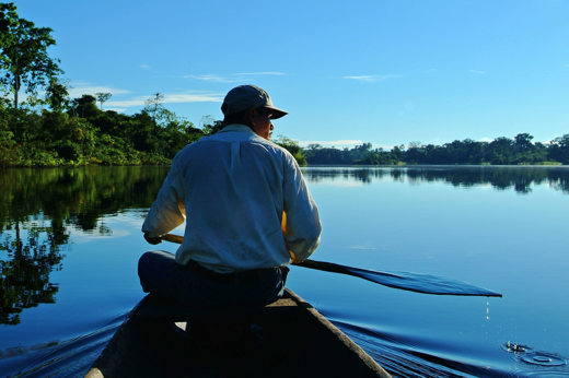 Local Amazon guide canoeing on a peaceful river at sunrise, surrounded by rainforest and reflections. 