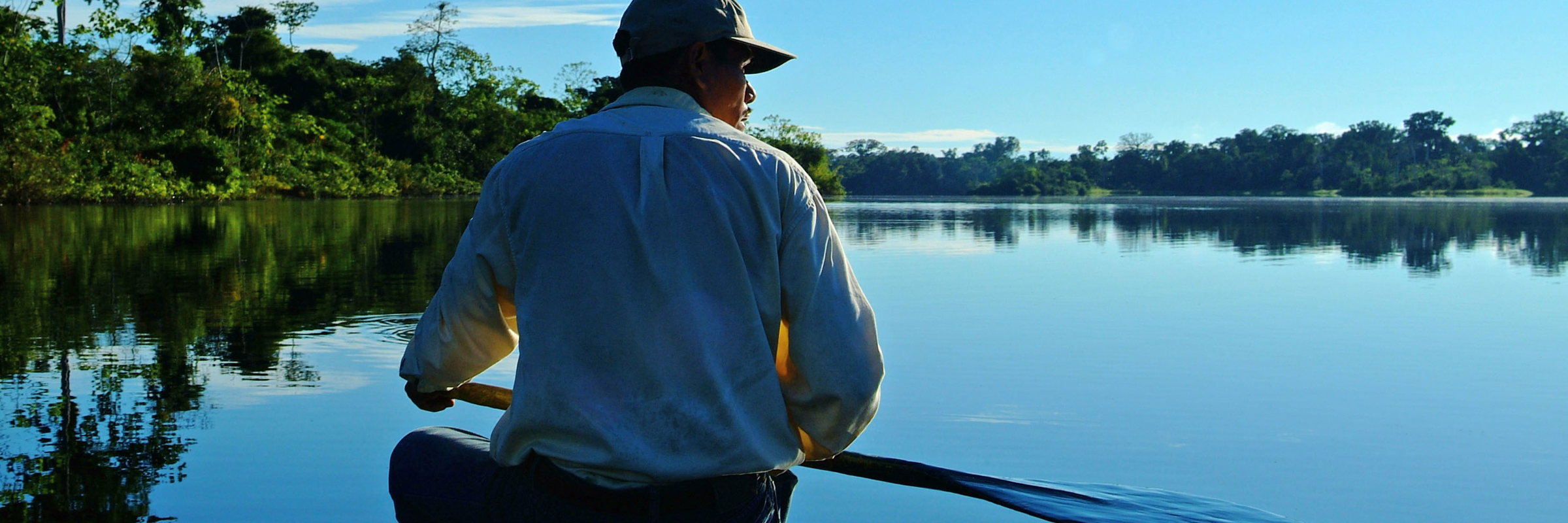 Local Amazon guide canoeing on a peaceful river at sunrise, surrounded by rainforest and reflections. 