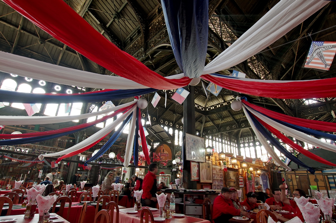 Decorated food hall in Santiago's Central Market, set for Chilean cooking experience with red-white-blue ribbons overhead. 