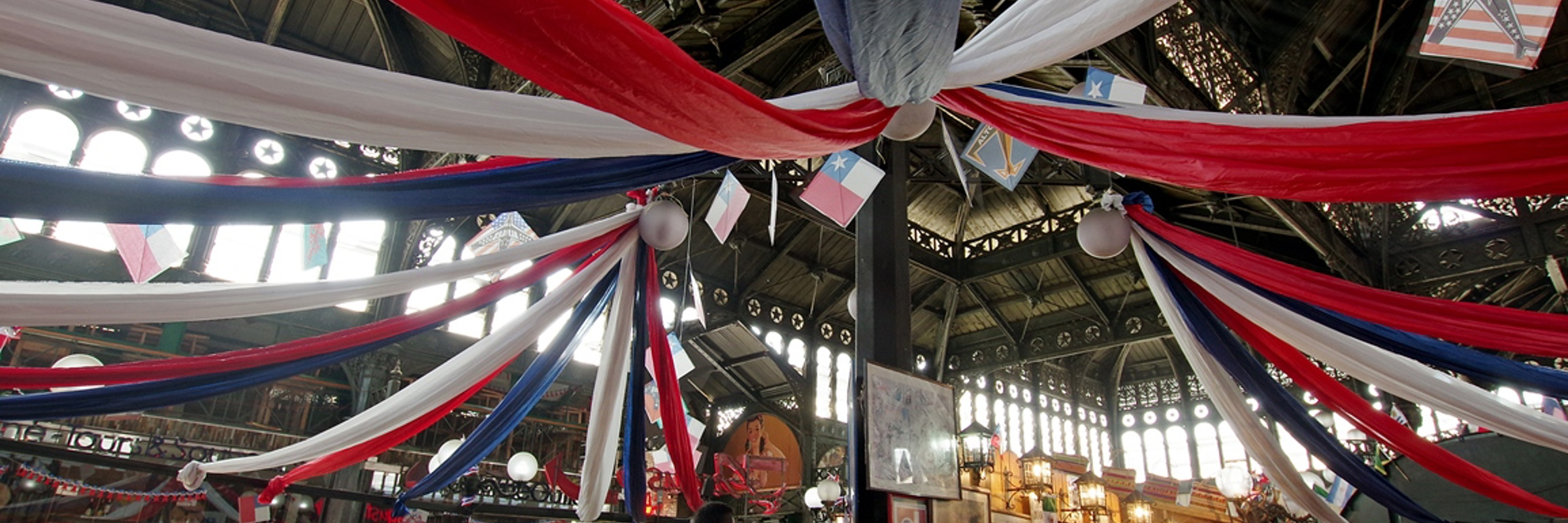 Decorated food hall in Santiago's Central Market, set for Chilean cooking experience with red-white-blue ribbons overhead. 