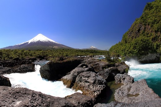 Petrohue Waterfalls cascade over volcanic rock with Osorno Volcano towering behind in Chile's Lake District, Northern Patagonia. 