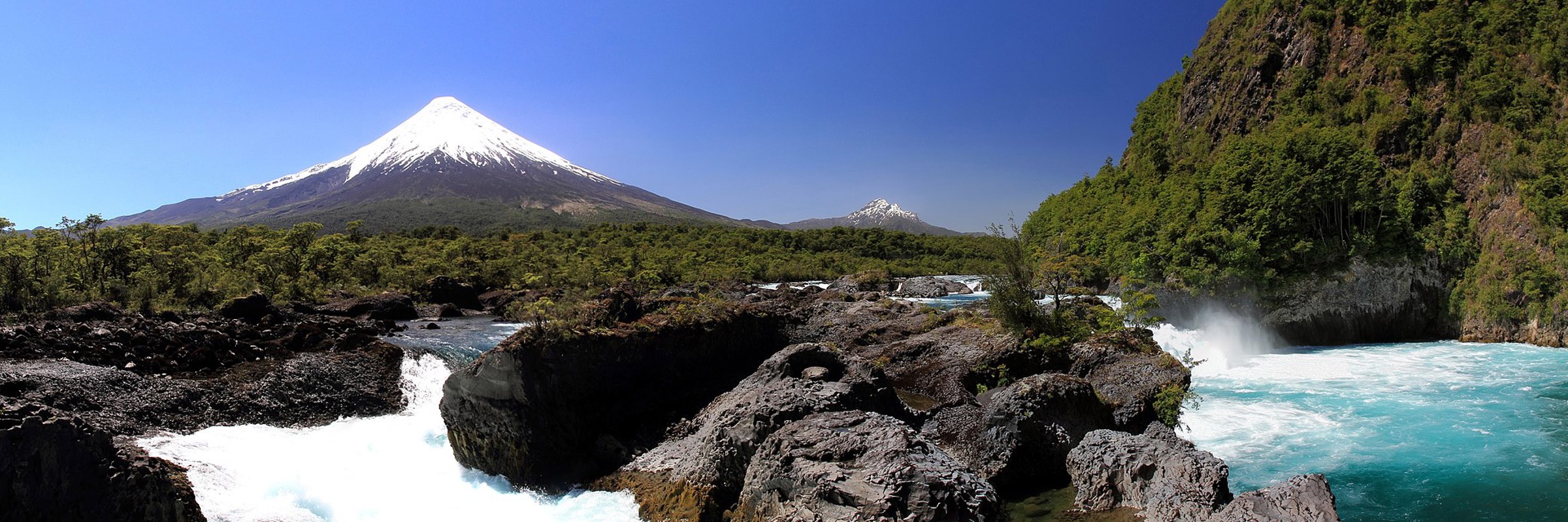 Petrohue Waterfalls cascade over volcanic rock with Osorno Volcano towering behind in Chile's Lake District, Northern Patagonia. 