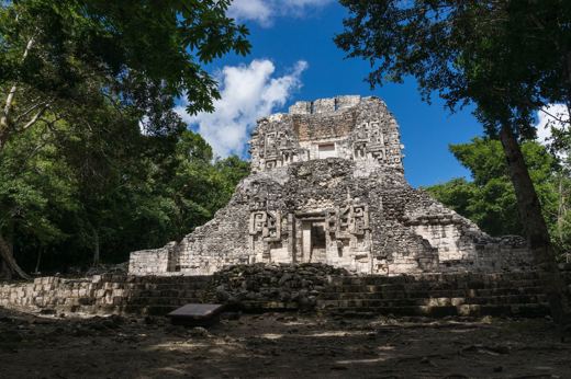 The main temple at Chicanna archaeological site, surrounded by jungle, featuring intricate Maya stucco decorations. 
