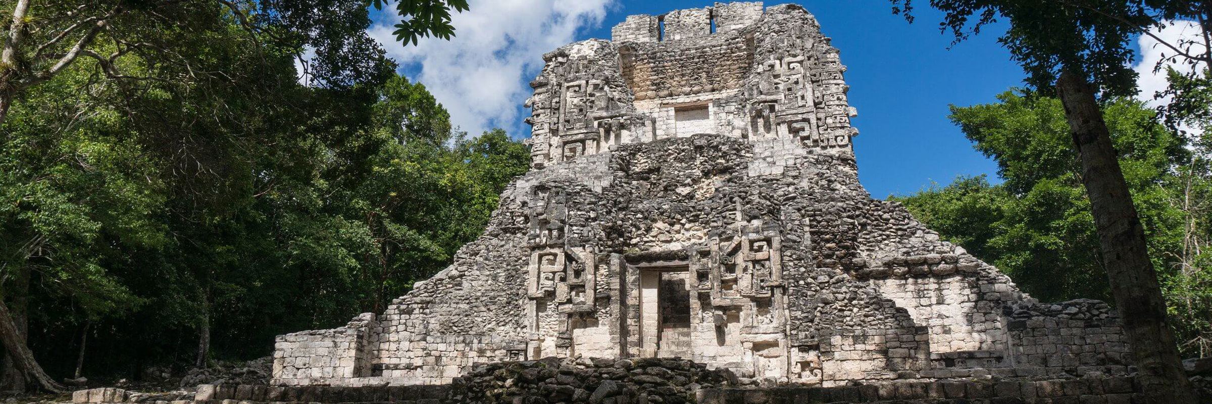 The main temple at Chicanna archaeological site, surrounded by jungle, featuring intricate Maya stucco decorations. 