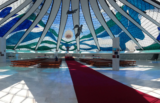 Interior of the Cathedral of Brasilia, showcasing stained glass ceiling and suspended angel sculptures in modernist design. 