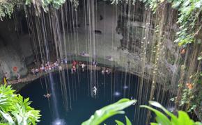 Visitors swim in the natural waters of Cenote Ik Kil, surrounded by hanging vines and limestone walls in Yucatan, Mexico. 
