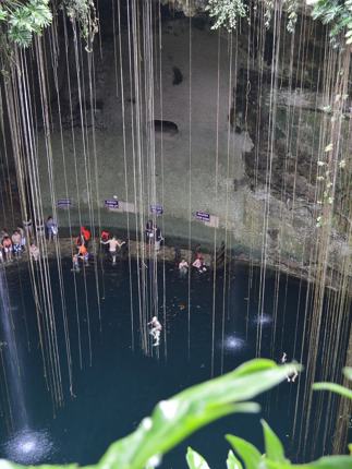 Visitors swim in the natural waters of Cenote Ik Kil, surrounded by hanging vines and limestone walls in Yucatan, Mexico. 
