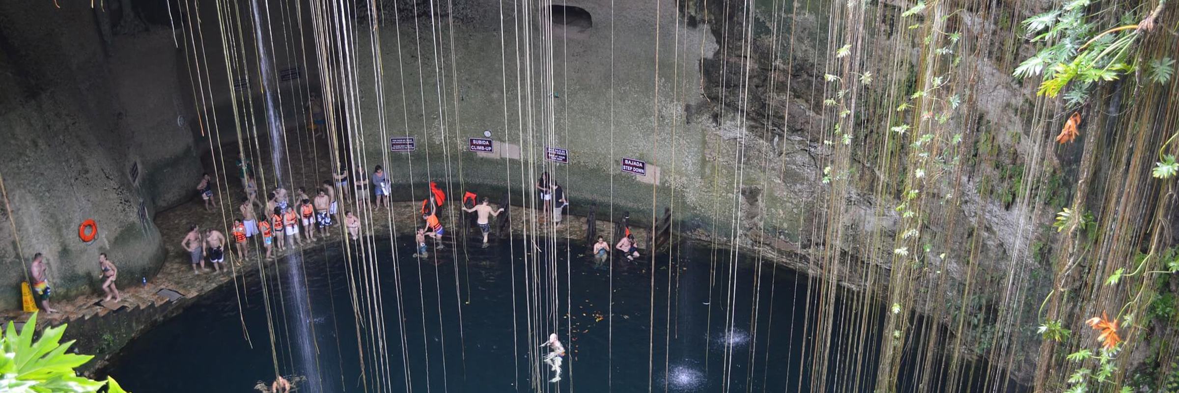 Visitors swim in the natural waters of Cenote Ik Kil, surrounded by hanging vines and limestone walls in Yucatan, Mexico. 
