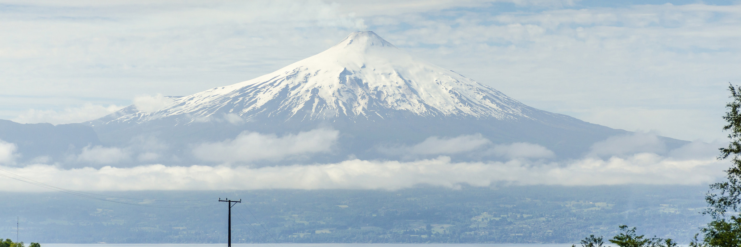 Villarrica Volcano with green meadows and cloud layers in Villarrica National Park, a highlight of southern Chile's Lake District. 
