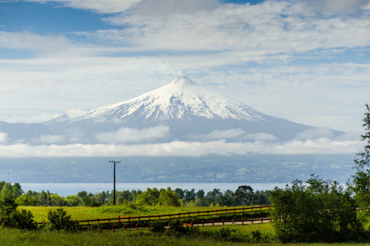 Villarrica Volcano with green meadows and cloud layers in Villarrica National Park, a highlight of southern Chile's Lake District. 
