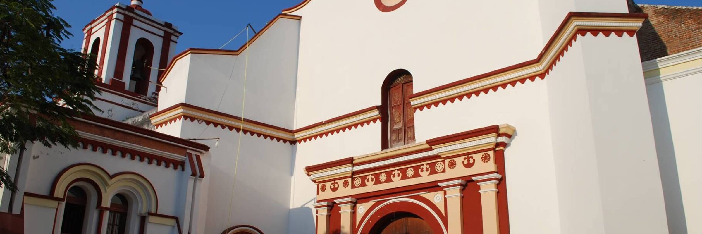Colonial-style church with white facade and red trim under a clear blue sky in Tehuantepec, Mexico. 