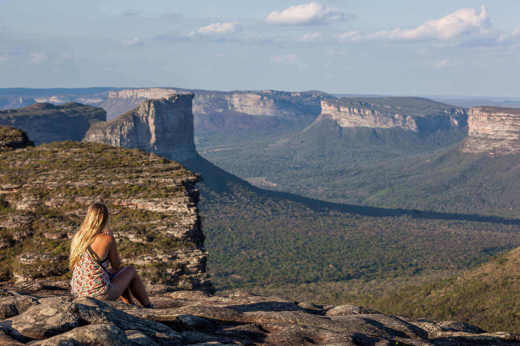 Woman sitting on cliff edge with panoramic views of mountains in Chapada Diamantina National Park, Brazil. 