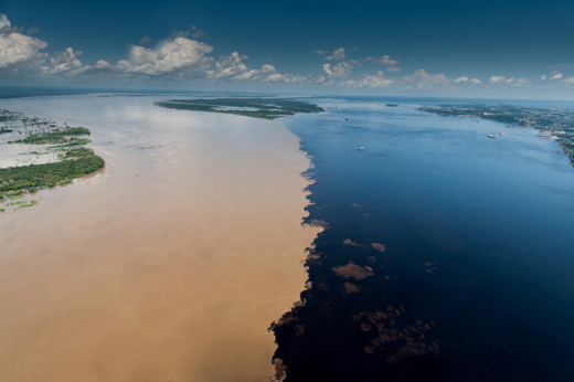 Aerial view of the Meeting of the Waters, where the dark Rio Negro and sandy Amazon River flow side by side without mixing. 