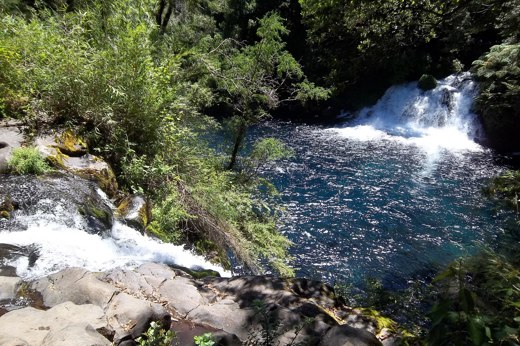 Caburgua waterfalls cascade into a clear blue pool surrounded by forest near Pucon in Chile's Lake District. 