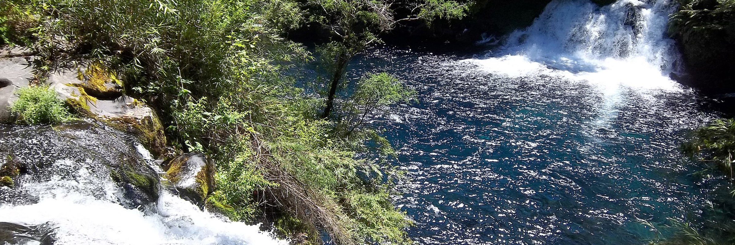 Caburgua waterfalls cascade into a clear blue pool surrounded by forest near Pucon in Chile's Lake District. 