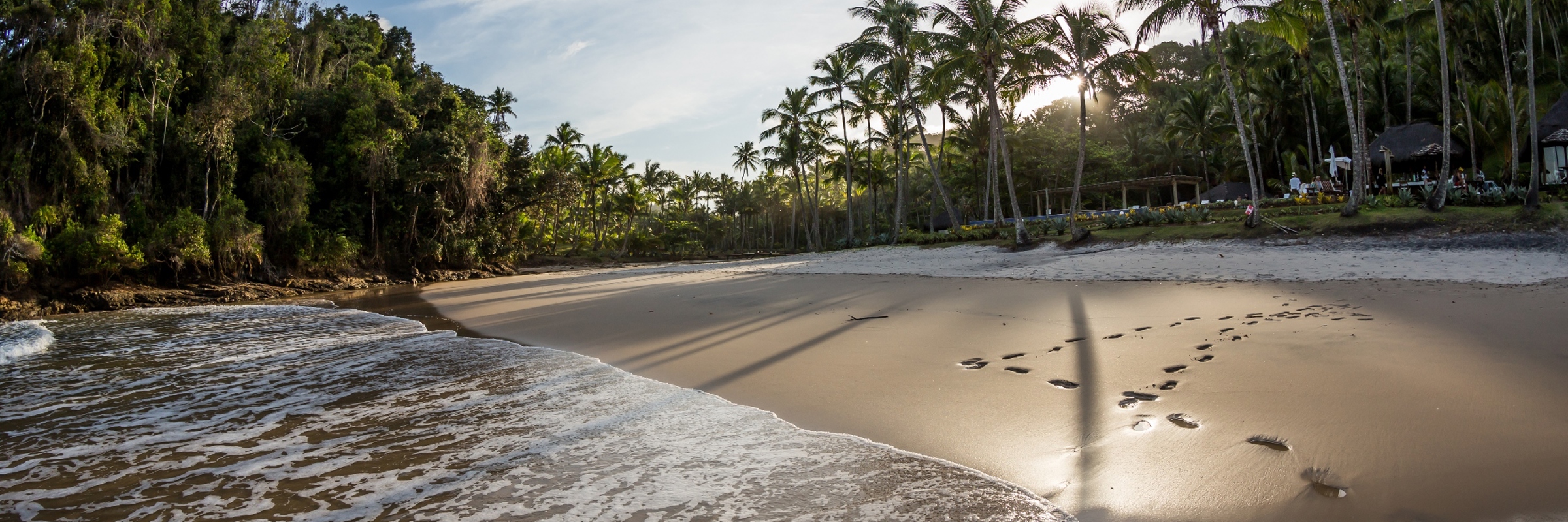 Secluded tropical beach in Brazil at sunset, with footprints in the sand and palm trees lining the coast. 