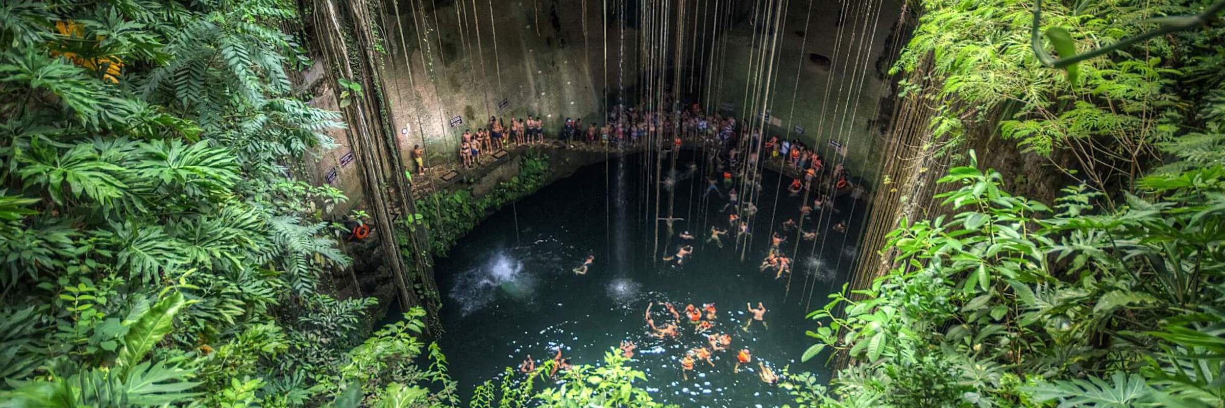 Cenote Ik Kil in Yucatan, Mexico, a deep natural sinkhole surrounded by lush jungle, vines, and clear blue swimming water. 