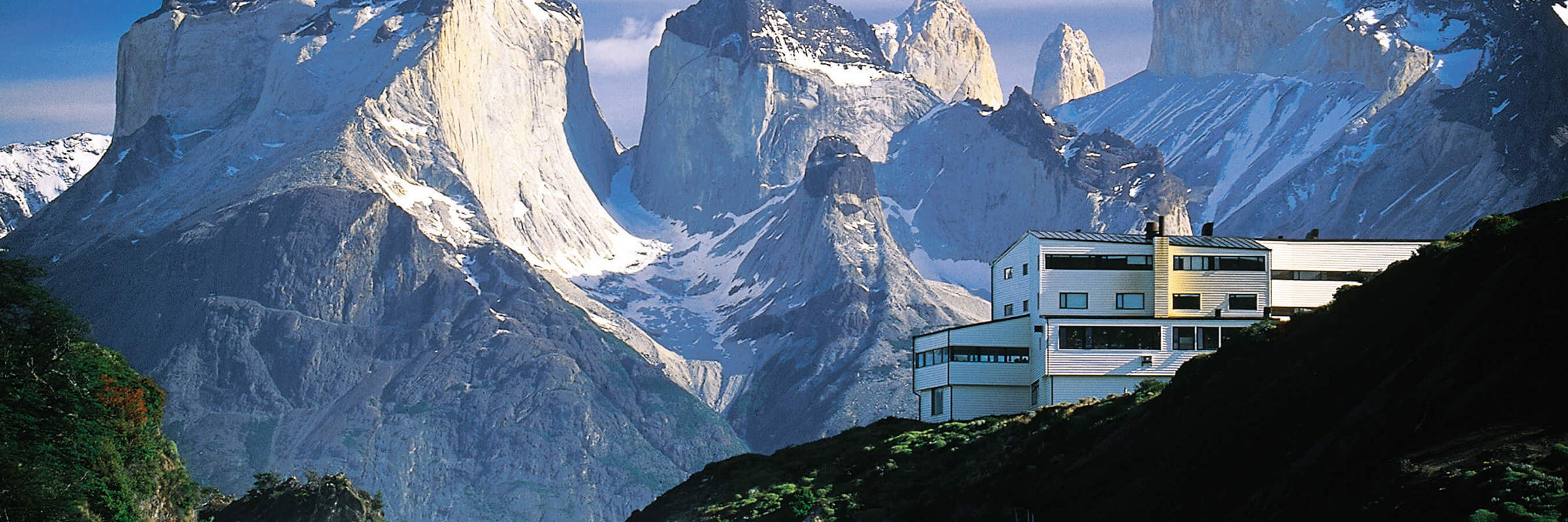 Explora Patagonia lodge nestled beside Salto Chico waterfall, with the dramatic peaks of Torres del Paine's Cuernos del Paine. 
