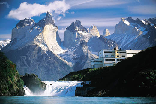 Explora Patagonia lodge nestled beside Salto Chico waterfall, with the dramatic peaks of Torres del Paine's Cuernos del Paine. 