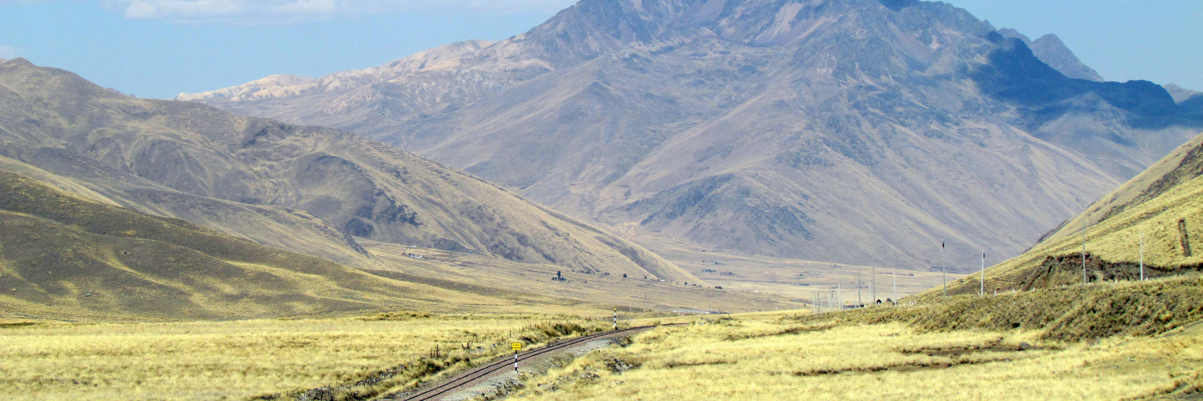 A quiet road winds through the rugged Peruvian Andes under a brilliant blue sky. 