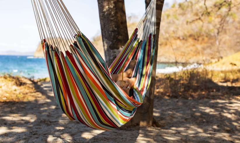 Relaxing in a colourful hammock strung between palm trees on a quiet tropical beach. 