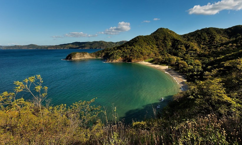 A tranquil bay framed by lush forested hills, offering stunning views of Costa Rica's unspoiled coastline. 