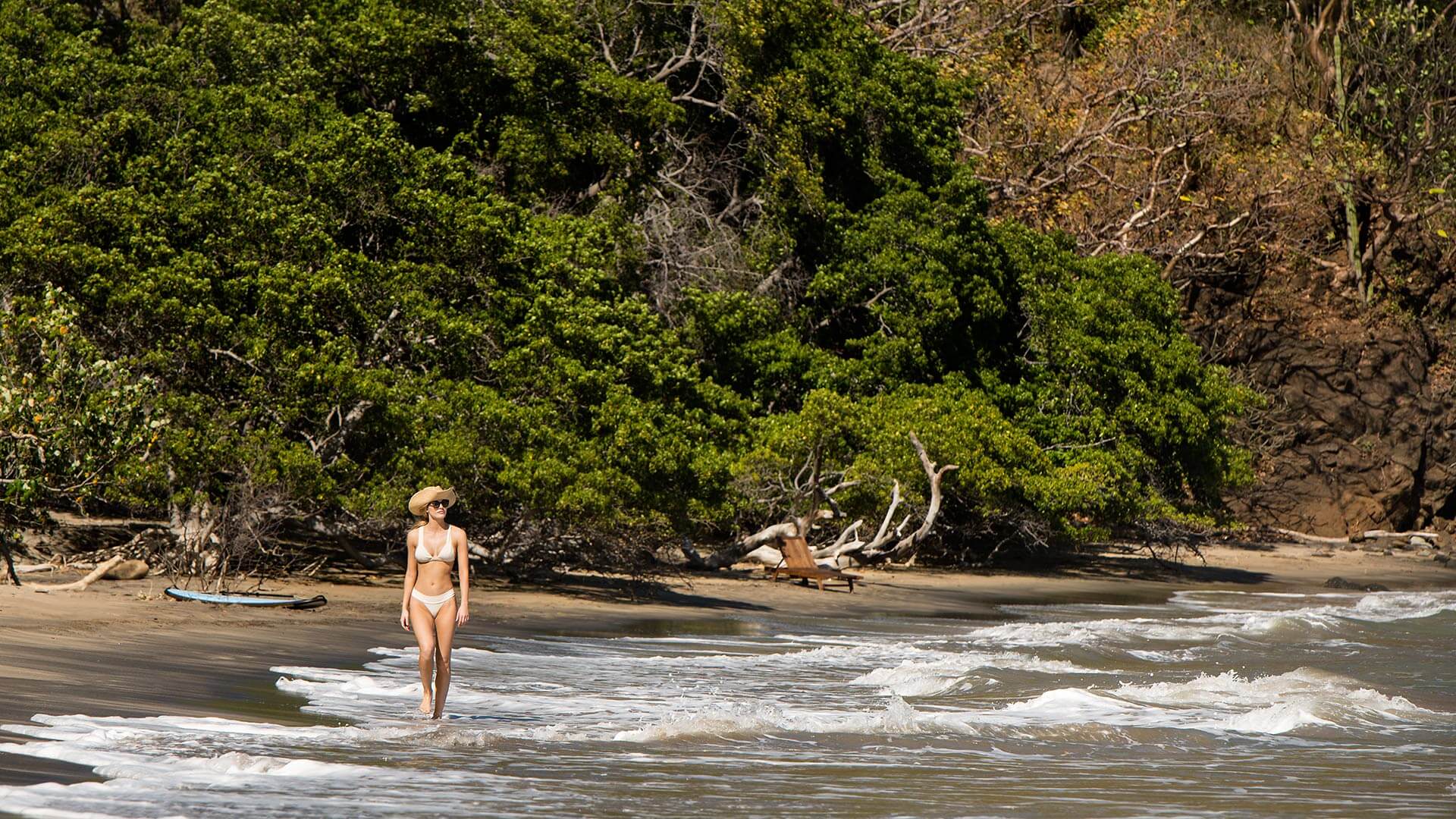 A woman strolls along a secluded beach backed by dense tropical forest at Kasiiya, embracing nature's calm. 