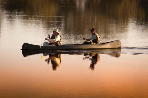 Two guests canoeing at sunrise in Caiman Ecological Refuge, Brazil, surrounded by calm reflective waters. 