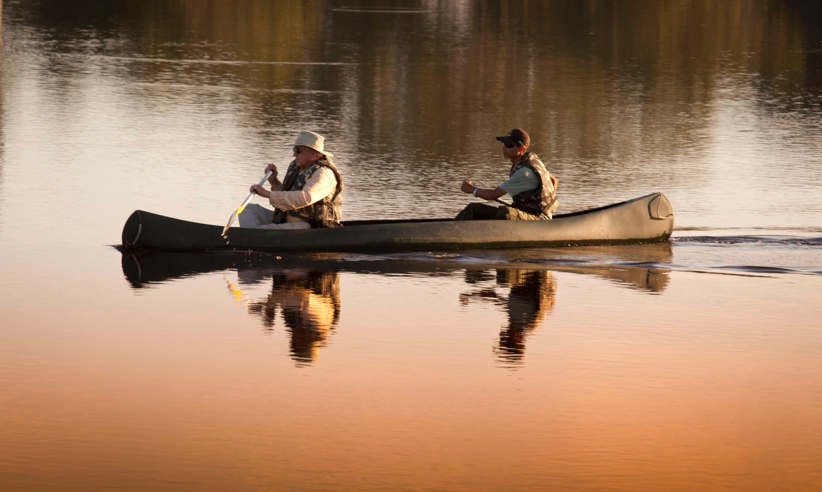 Two guests canoeing at sunrise in Caiman Ecological Refuge, Brazil, surrounded by calm reflective waters. 