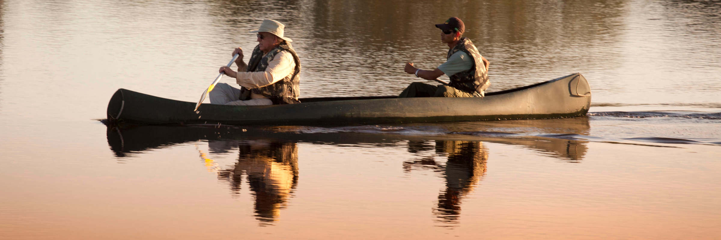 Two guests canoeing at sunrise in Caiman Ecological Refuge, Brazil, surrounded by calm reflective waters. 