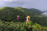 Adventurers ziplining high above the rainforest canopy with misty mountains in the background. 