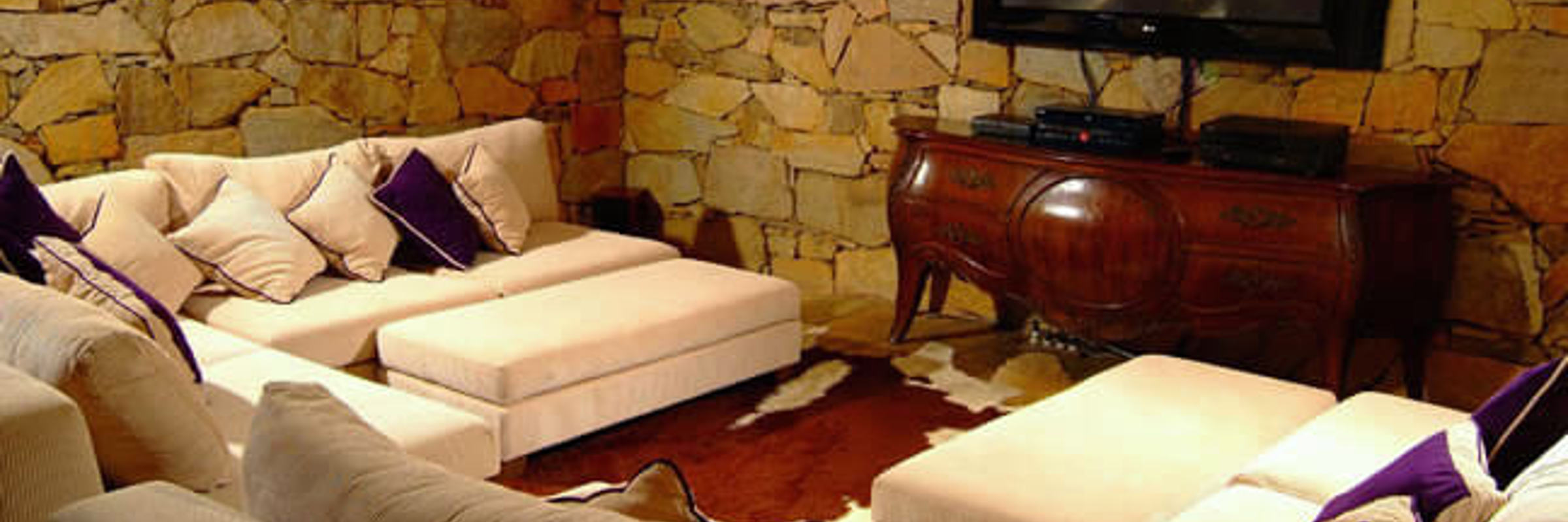 Cozy Ingenuity Room with plush seating, stone walls, and TV at Ibitipoca Reserve, Brazil. 