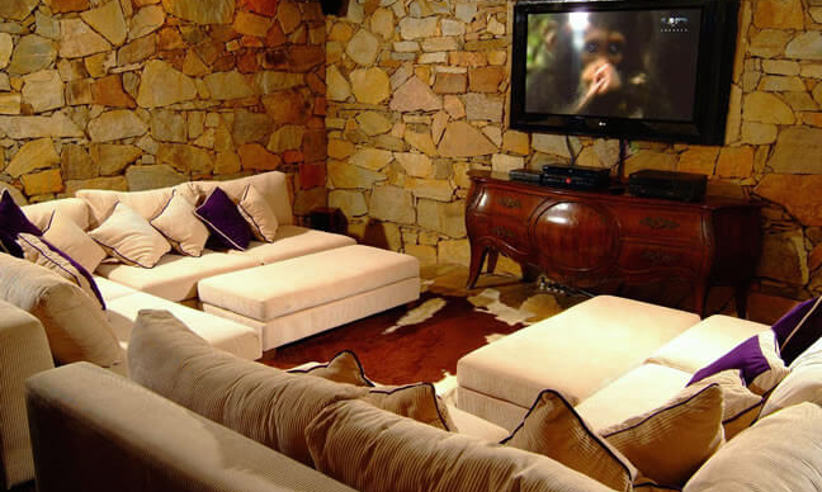 Cozy Ingenuity Room with plush seating, stone walls, and TV at Ibitipoca Reserve, Brazil. 