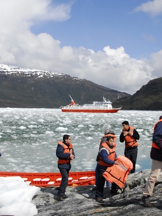 Tourists in life jackets disembark from Zodiacs onto an icy shoreline during a glacier expedition cruise in Chilean Patagonia. 