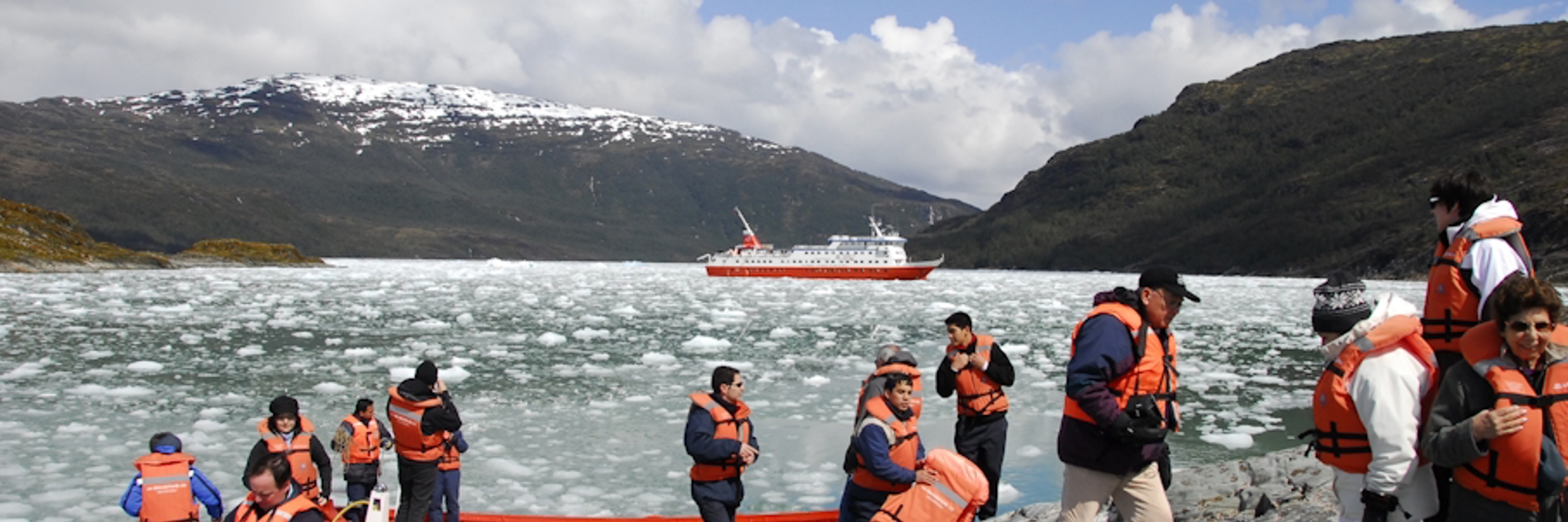 Tourists in life jackets disembark from Zodiacs onto an icy shoreline during a glacier expedition cruise in Chilean Patagonia. 