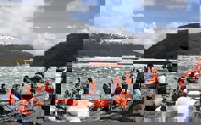 Tourists in life jackets disembark from Zodiacs onto an icy shoreline during a glacier expedition cruise in Chilean Patagonia. 
