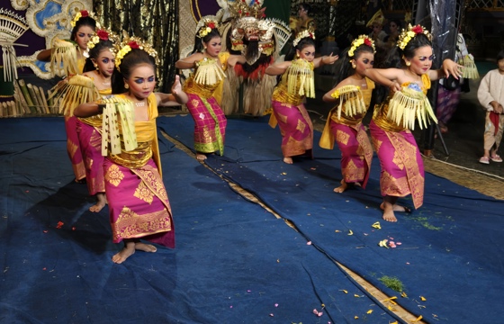 Young Balinese girls in vibrant costumes perform a traditional dance with elegant gestures on a decorated stage. 