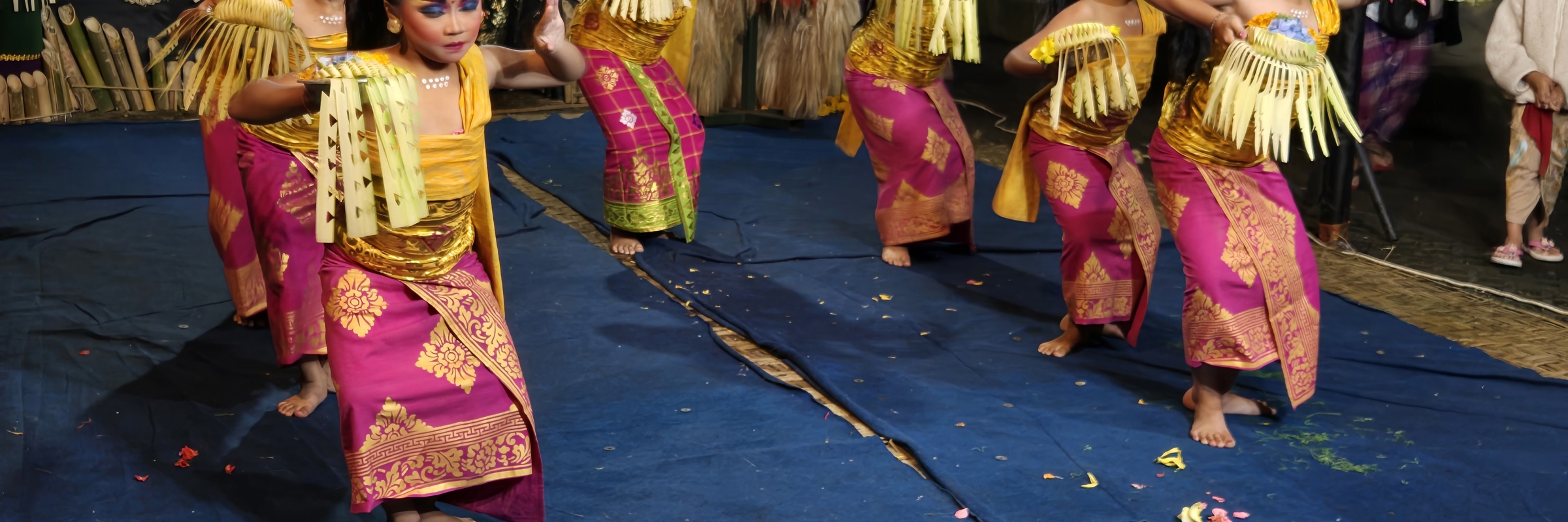 Young Balinese girls in vibrant costumes perform a traditional dance with elegant gestures on a decorated stage. 