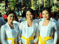 Three Balinese women in white kebaya and yellow sashes during a temple ceremony in Ubud, Bali. 