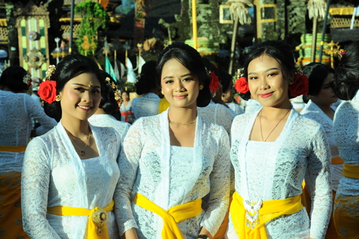Three Balinese women in white kebaya and yellow sashes during a temple ceremony in Ubud, Bali. 