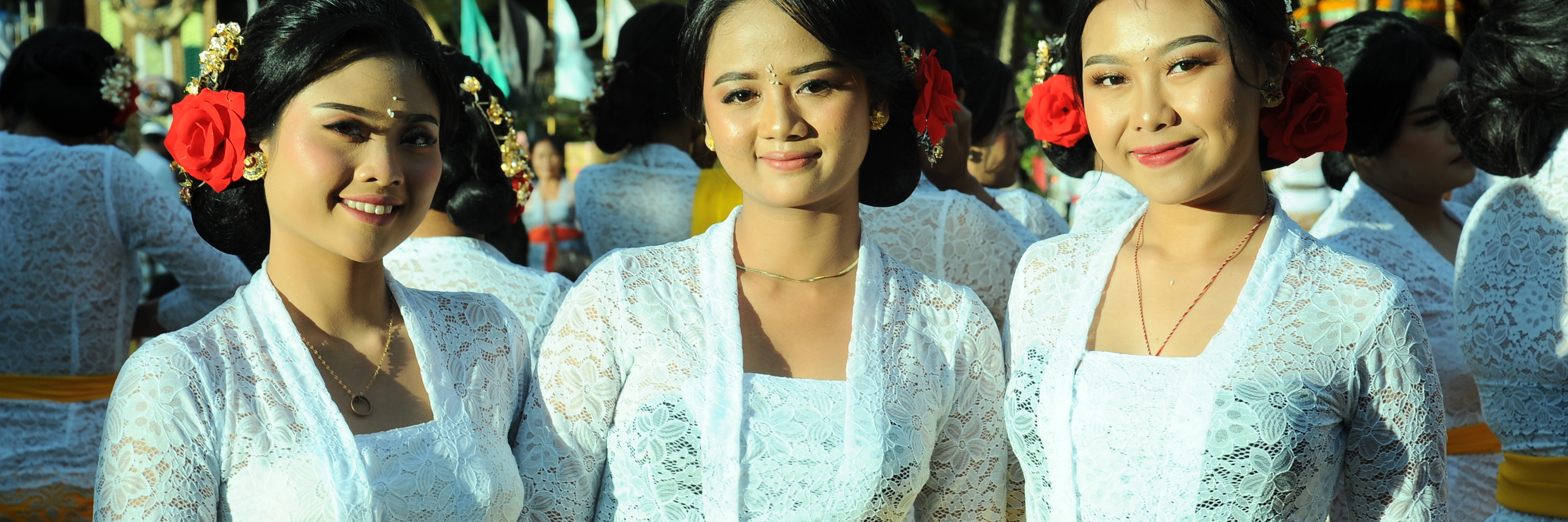 Three Balinese women in white kebaya and yellow sashes during a temple ceremony in Ubud, Bali. 